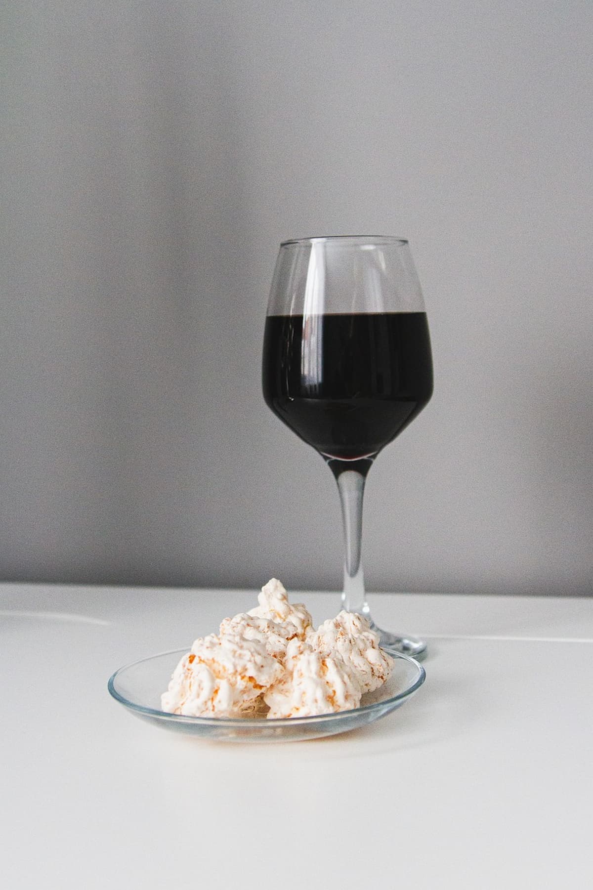 Uma taça de vinho em uma mesa branca, junto com uma prato com doces