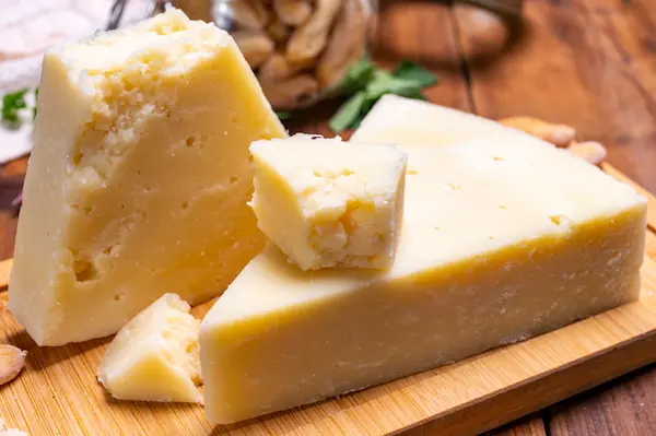 Pedaços de queijo Pecorino Romano sobre tábua de madeira, ingrediente tradicional utilizado na receita de macarrão à carbonara.
