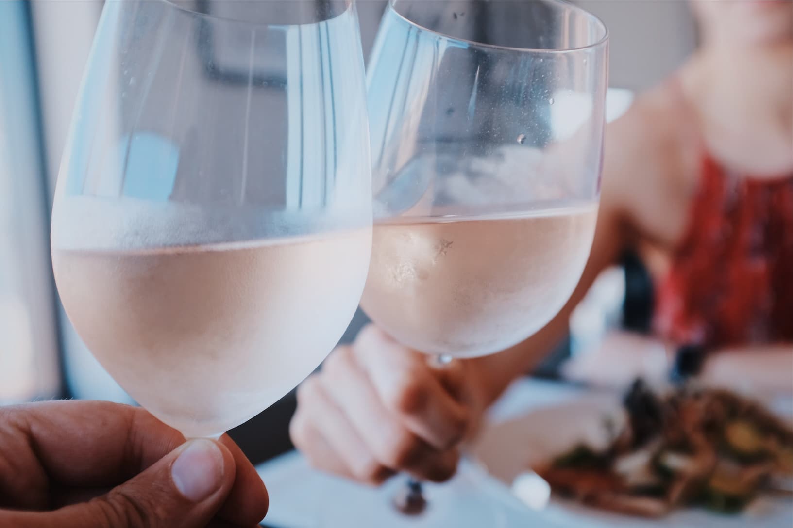 Um homem e uma mulher brindam com vinho rosé durante o almoço. Imagem disponível em unsplash.