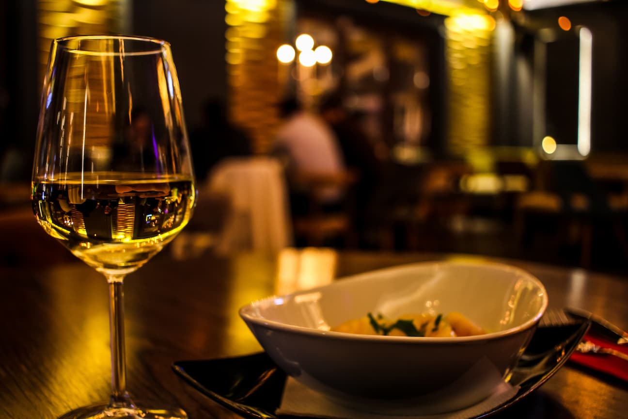 Taça de vinho verde ao lado de um prato. Imagem disponível em Pexels.