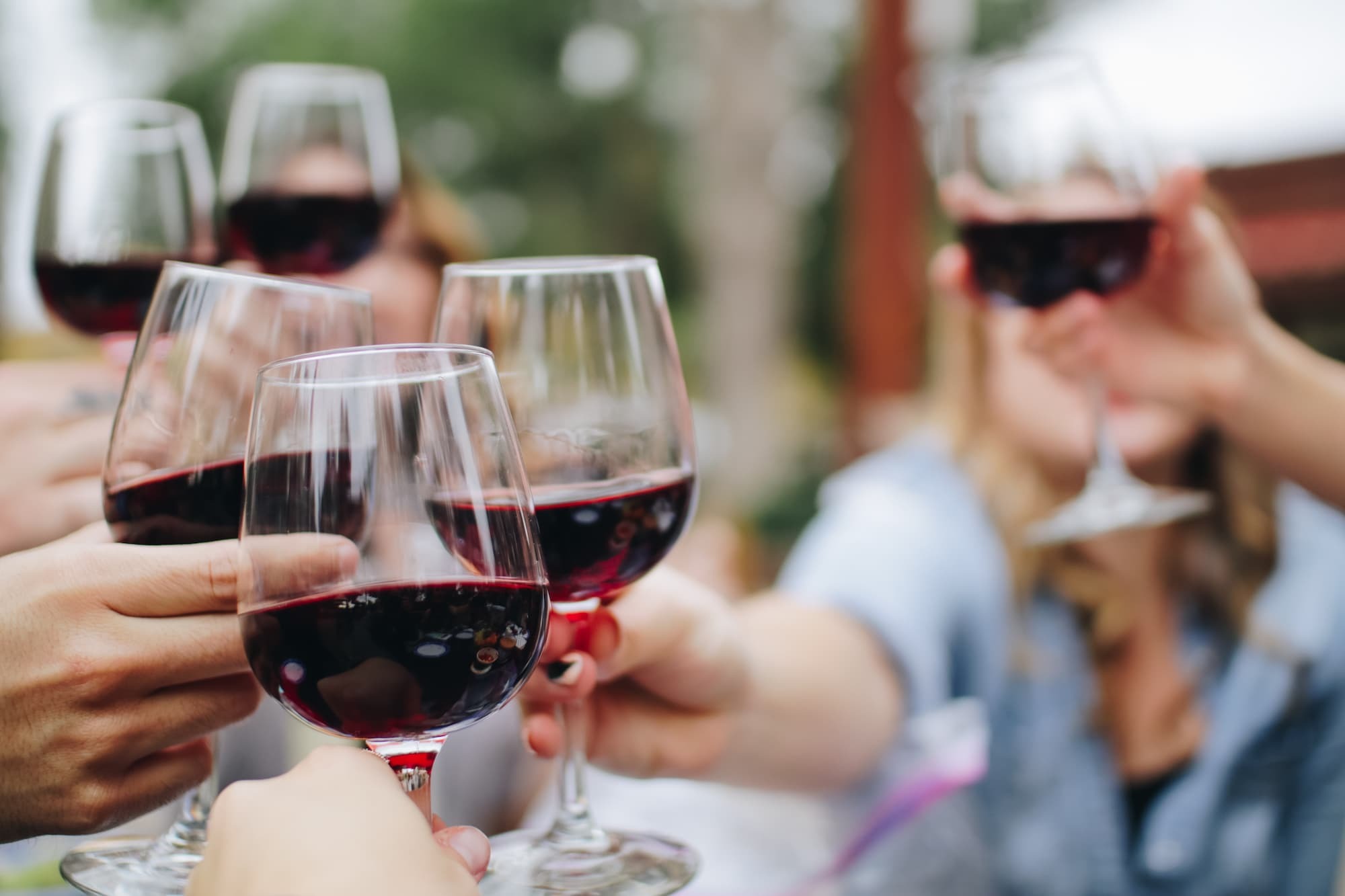 Pessoas brindam com vinho tinto. Imagem disponível em Unsplash.