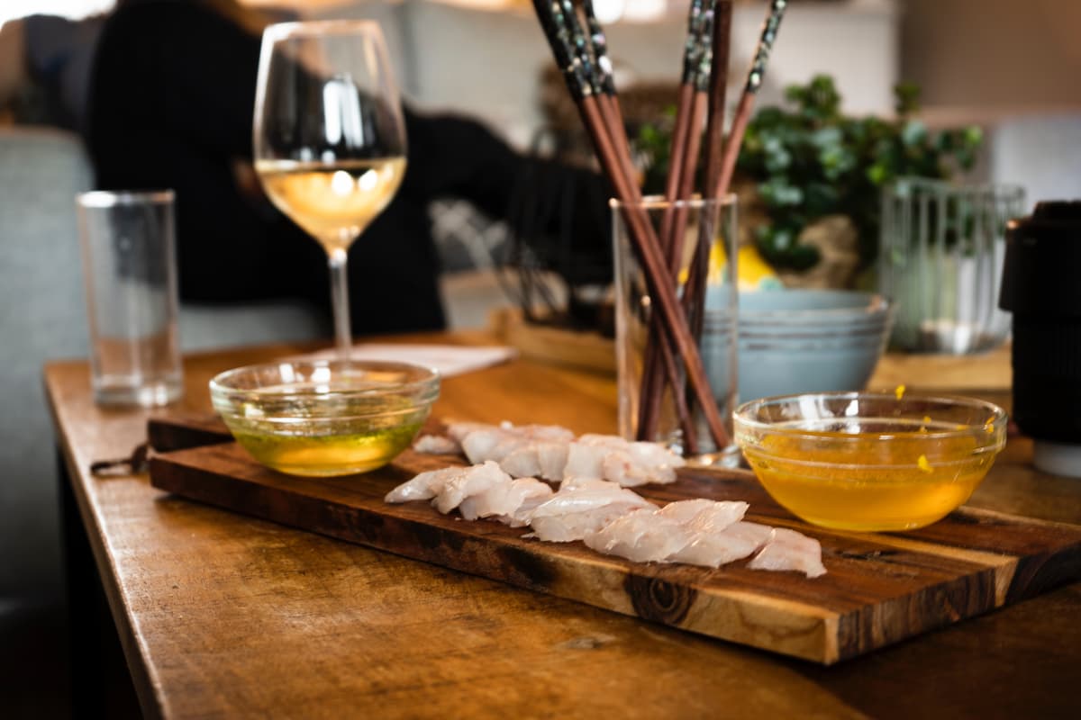 Uma taça de vinho branco servida ao lado de uma bandeja de comida japonesa.