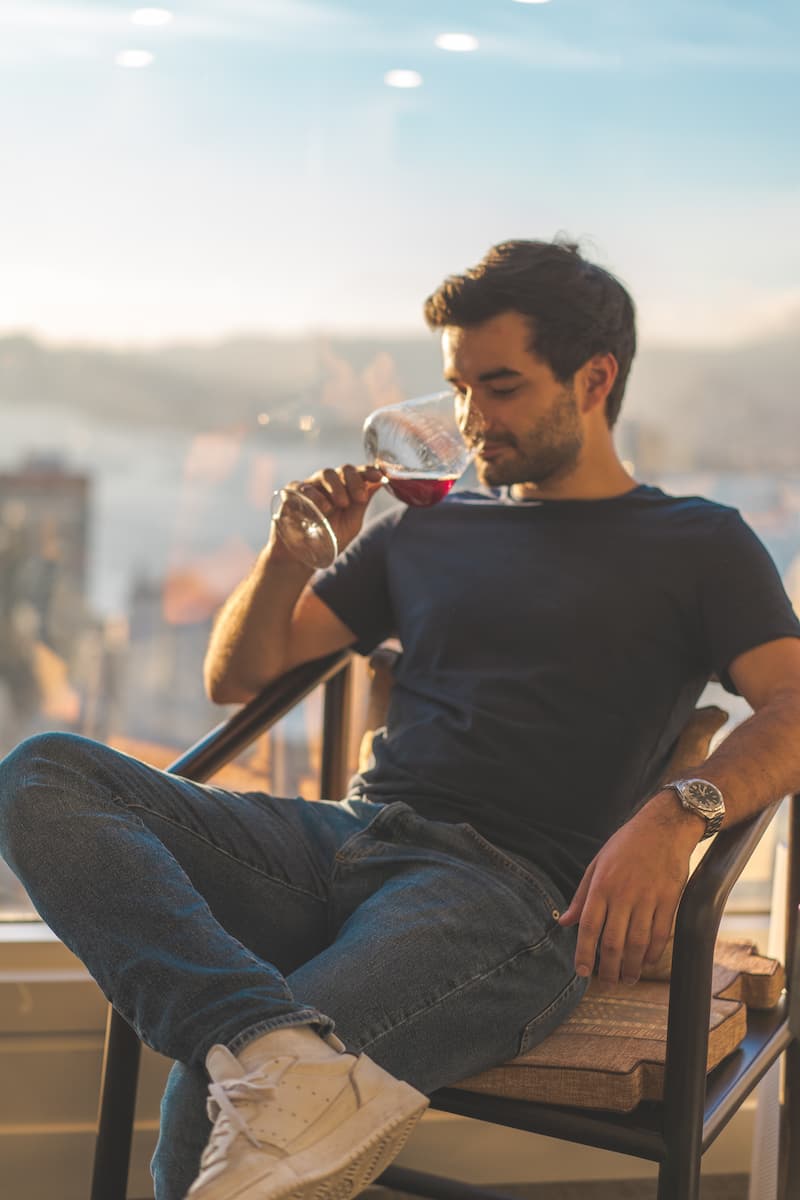 Homem, em uma varanda, aprecia uma taça de vinho tinto.
