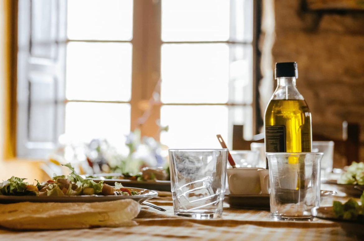 Mesa posta com azeite, copos transparentes e pratos de salada.
