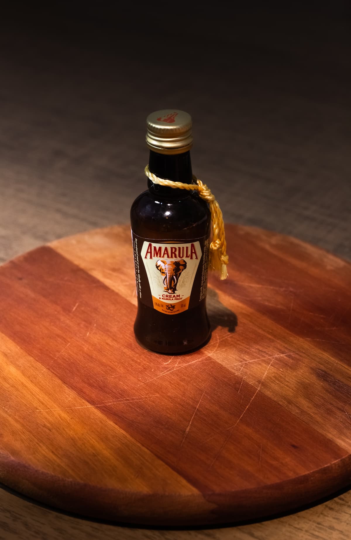 Uma garrafa pequena de amarula em uma tábua de madeira redonda 