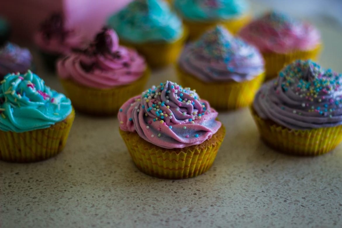 Uma mesa com vários cupcakes cloridos.