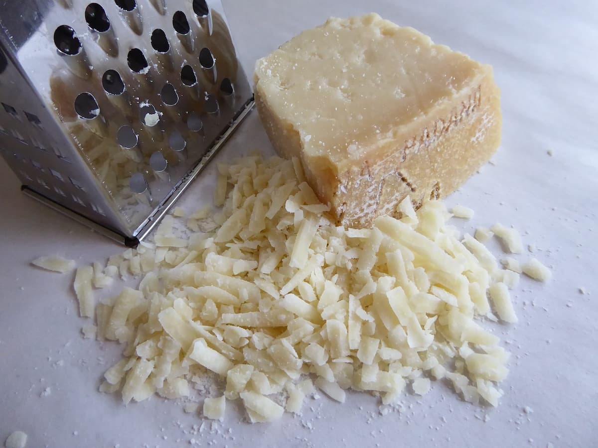 Um queijo parmesão em cima de mesa junto com um ralador de queijo.