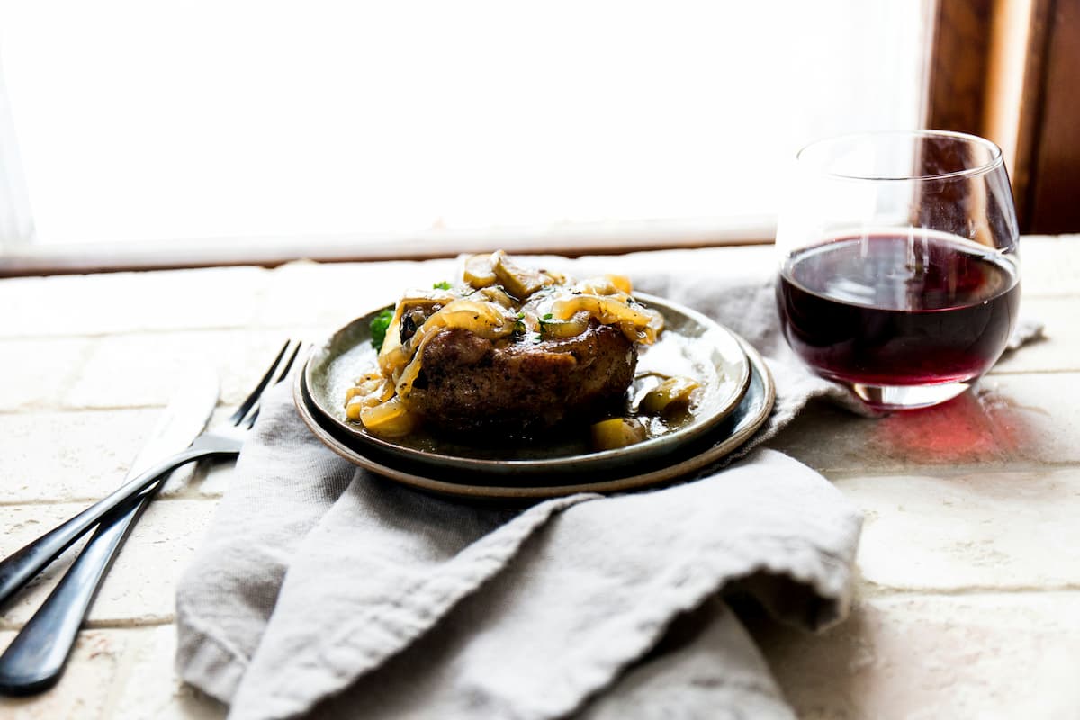 Um prato de rosbife em uma mesa acompanhado de um copo de vinho