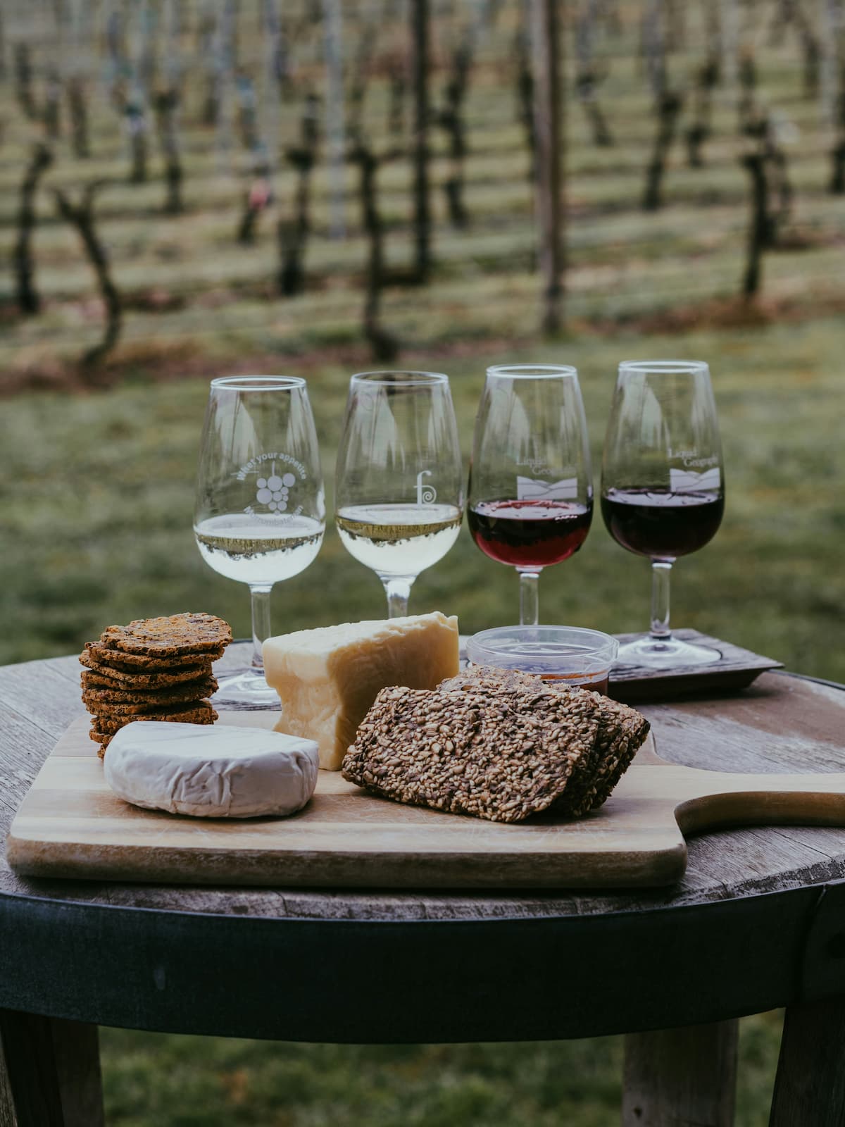 Quatro taças de vinho em uma mesa junto com pães em uma badeja de madeira
