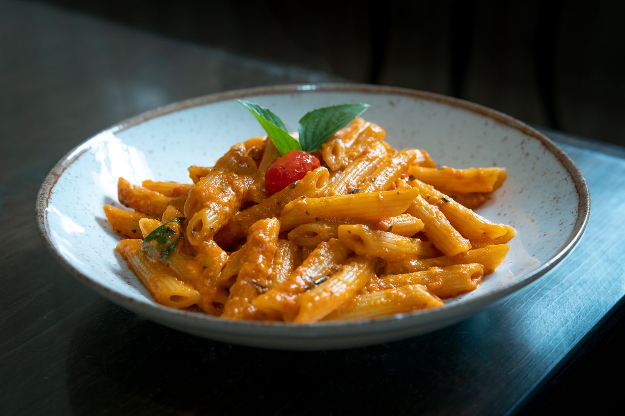 Macarrão penne ao molho cremoso de tomate, decorado com tomate-cereja e folhas de manjericão.