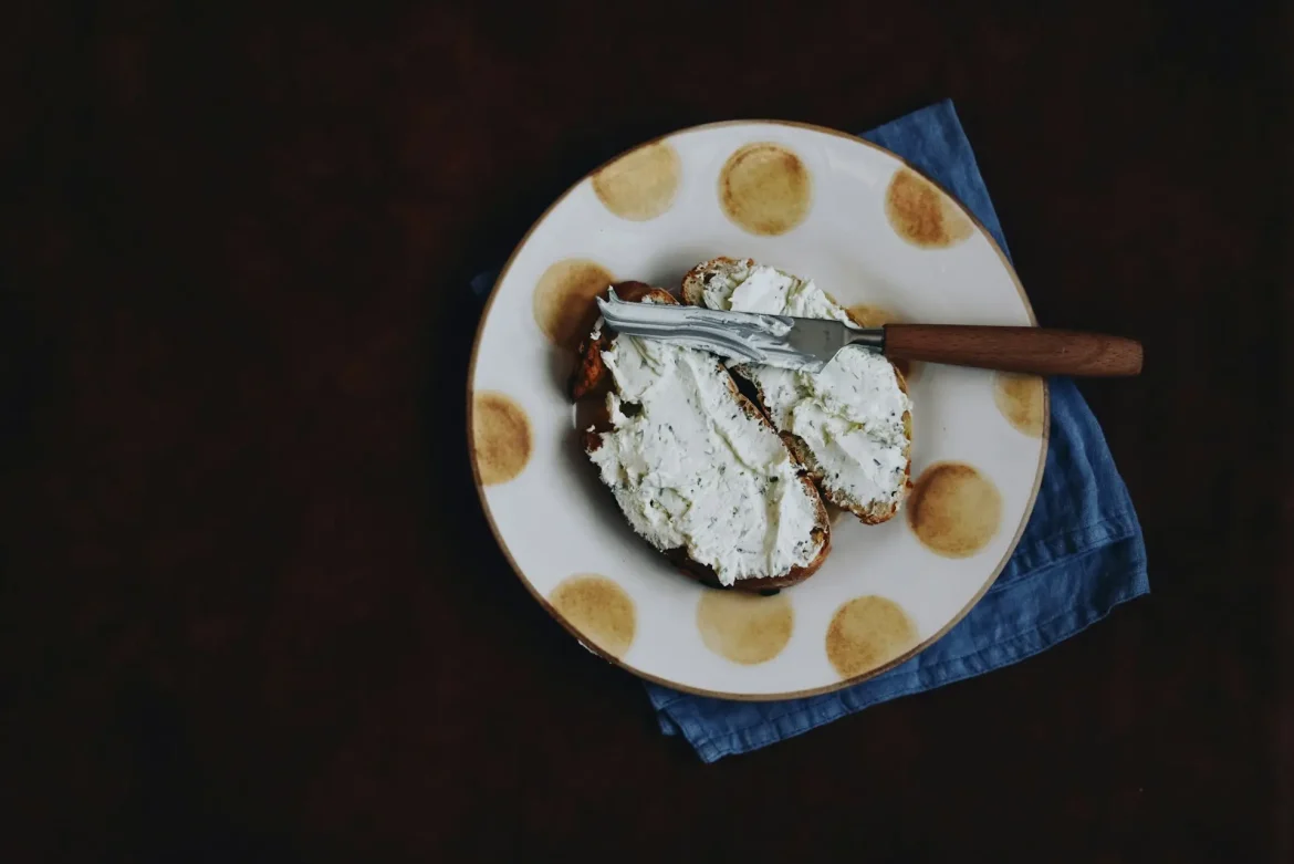 Queijo mascarpone espalhado sobre fatias de pão em um prato, acompanhado de uma faca.