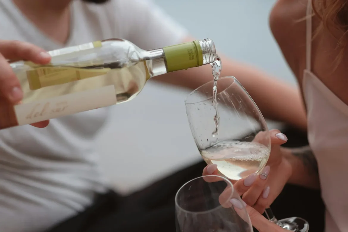 Pessoa servindo vinho branco em uma taça durante uma confraternização.